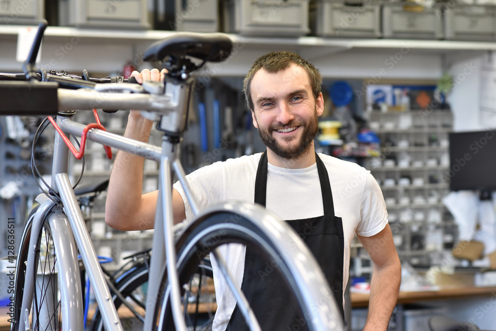 Freundlicher Zweiradmechatroniker in einer Fahrradwerkstatt repariert Räder