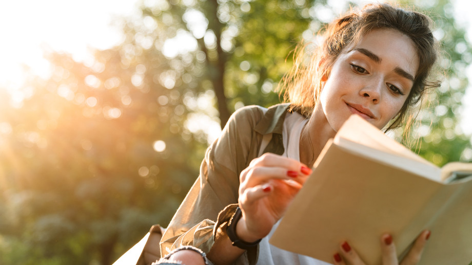 Junge Frau, die im grünen Park ein Buch liest und lächelt