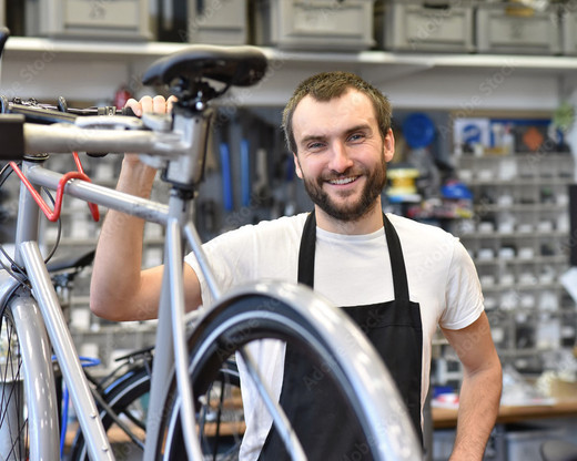 Freundlicher Zweiradmechatroniker in einer Fahrradwerkstatt repariert Räder