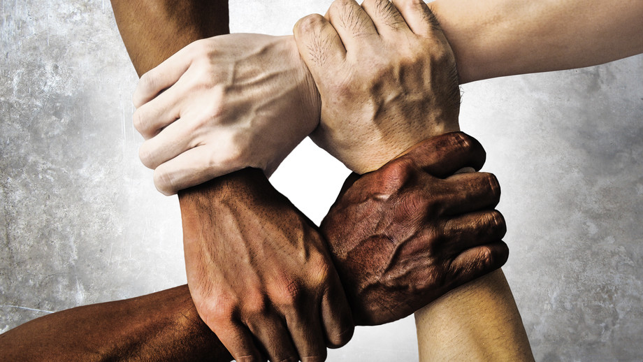 Vier Hände halten sich gegenseitig in einem Kreis am Handgelenk fest. Die Personen besitzen alle unterschiedliche Hautfarben.